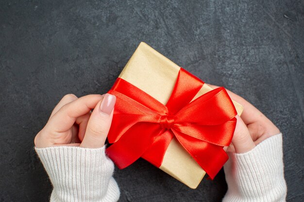 Draufsicht der Hand, die schönes Geschenk mit bogenförmigem Band auf dunklem Hintergrund hält