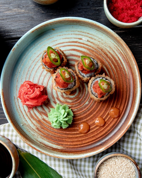 Draufsicht der heißen gebratenen Sushi-Rollen mit Wasabi und Ingwer auf einem Teller auf Holz