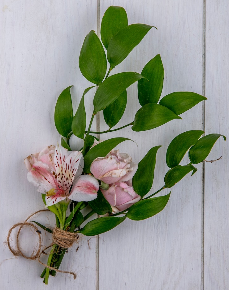 Kostenlose Foto draufsicht der hellrosa rose mit einem zweig der blätter und einer lilie auf einer grauen oberfläche