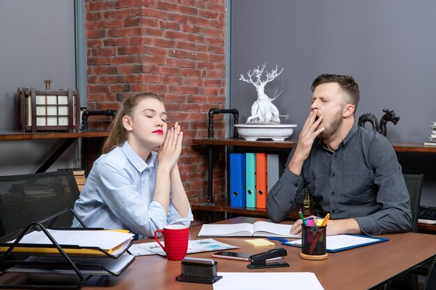 Draufsicht der jungen Arbeiterin und ihres männlichen Mitarbeiters, der müde am Tisch im Büro sitzt