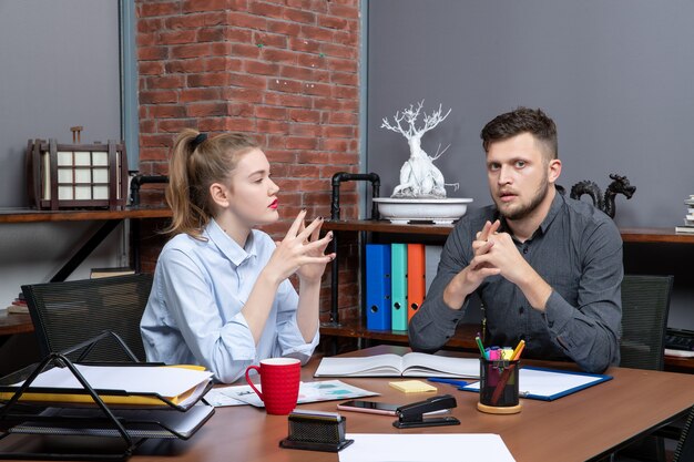 Draufsicht der jungen Arbeiterin und ihres männlichen Mitarbeiters, die am Tisch sitzen und ein wichtiges Thema in der Büroumgebung diskutieren