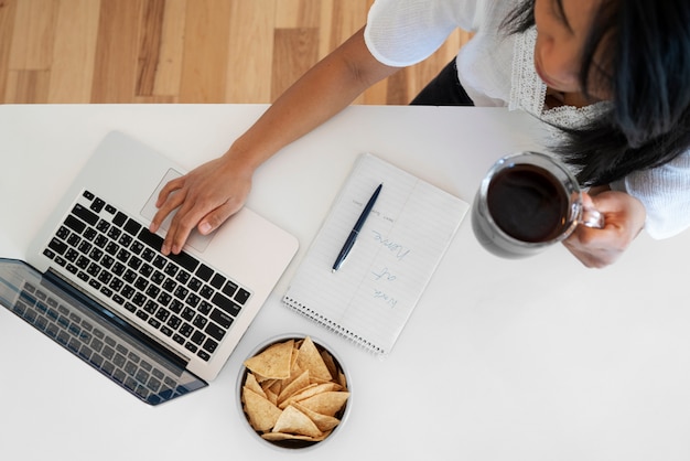 Draufsicht der jungen Frau, die Laptop verwendet und eine Tasse Kaffee trinkt