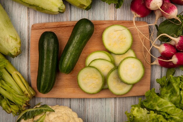 Draufsicht der kalorienarmen Gurken auf einem hölzernen Küchenbrett mit Radieschen-Zucchini und Sellerie lokalisiert auf einer grauen Holzoberfläche