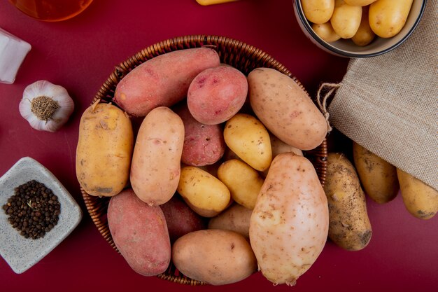 Draufsicht der Kartoffeln im Korb mit Salz des schwarzen Pfeffersamen des Knoblauchs auf Bordooberfläche