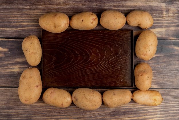 Kostenloses Foto draufsicht der kartoffeln um leere schale auf holz