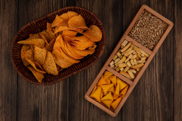 Kostenloses Foto draufsicht der kegelform-signalhorn-chips auf einem geteilten holzteller mit geschälten sonnenblumenkernen mit würzigen chips auf einem eimer auf einer holzwand