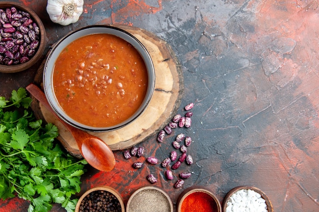 Draufsicht der klassischen Tomatensuppe in einem blauen Schüssellöffel auf hölzernem Tablett Knoblauch und einem Bündel Grün auf Mischfarbtabelle