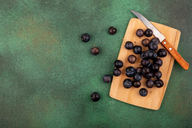 Draufsicht der kleinen sauren blau-schwarzen Fruchtschleifen auf einem hölzernen Küchenbrett mit Messer auf einem grünen Hintergrund mit Kopienraum