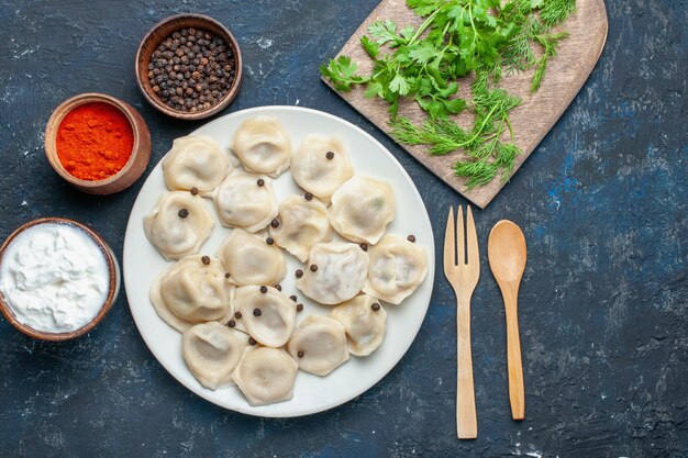 Draufsicht der köstlichen gebackenen Knödel innerhalb des Tellers zusammen mit Pfeffer und Grün auf dunklem Schreibtisch, Teigmahlzeitnahrungsmittelessen-Fleischkalorie