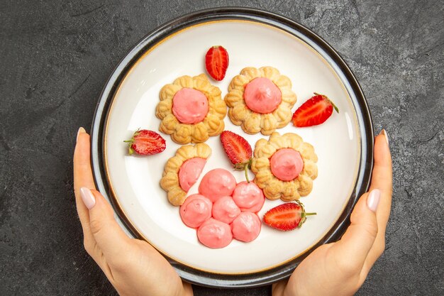 Draufsicht der köstlichen kleinen Kekse mit rosa Creme-Innenplatte auf dunkelgrauer Oberfläche