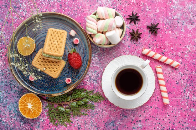 Draufsicht der köstlichen Waffeln mit Tasse Tee und Eibisch auf rosa Schreibtisch