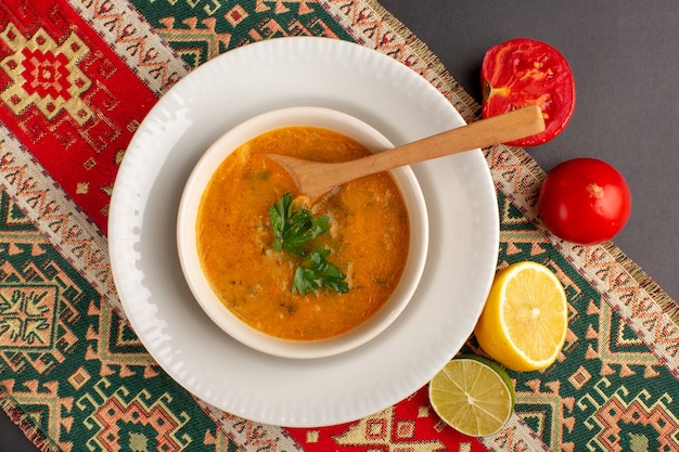 Kostenloses Foto draufsicht der leckeren gemüsesuppe innerhalb platte mit tomaten und zitrone auf dunkler oberfläche