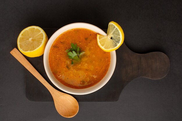 Draufsicht der leckeren Gemüsesuppe innerhalb Platte zusammen mit Zitrone auf der dunklen Oberfläche