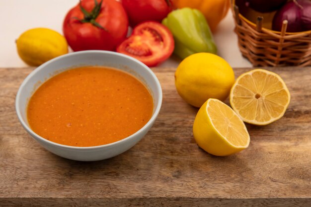 Draufsicht der leckeren Linsensuppe auf einer Schüssel auf einem hölzernen Küchenbrett mit Zitronen mit roten Zwiebeln auf einem Eimer mit Tomaten und Paprika isoliert auf einer weißen Oberfläche