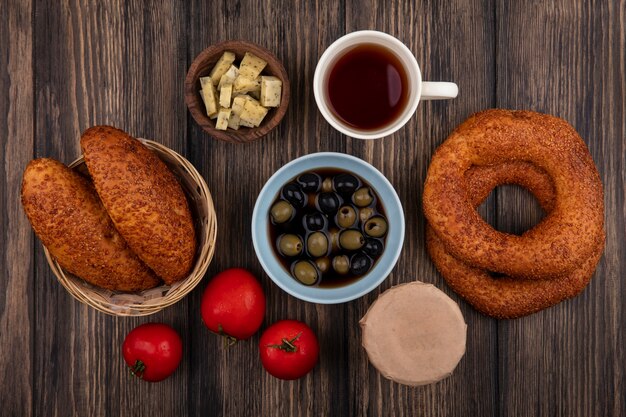 Draufsicht der leckeren türkischen Bagels mit Pastetchen auf einem Eimer mit Oliven auf einer Schüssel mit einer Tasse Tee und Tomaten lokalisiert auf einem hölzernen Hintergrund