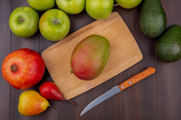 Draufsicht der Mango auf einem hölzernen Küchenbrett mit Messer mit Apfelgranatapfel auf einer hölzernen Oberfläche