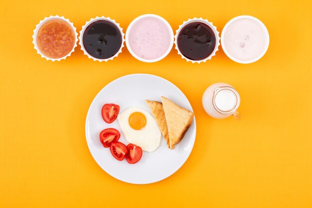 Draufsicht der Marmelade mit Joghurt und Spiegelei auf gelber Fläche horizontal