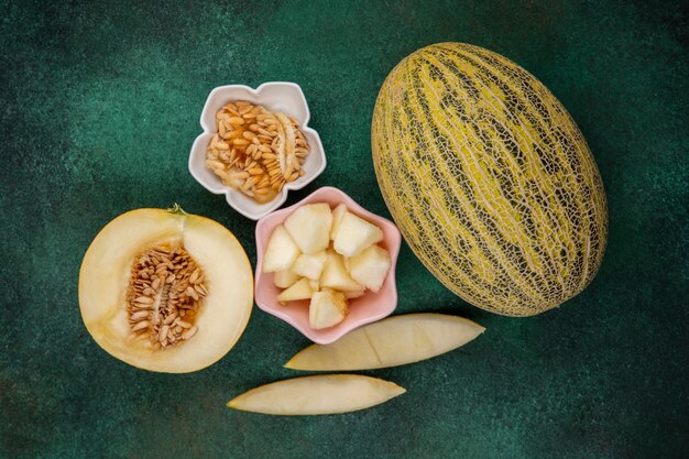 Draufsicht der Melone mit Scheiben auf einer rosa Schüssel mit Melonenschalen auf grüner Oberfläche