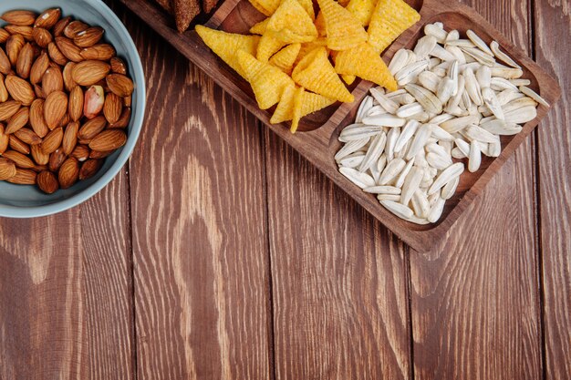 Draufsicht der Mischung aus salzigen Biersnacks, Sonnenblumenkernen, Maiskegeln und Mandeln auf rustikalem Holz mit Kopierraum