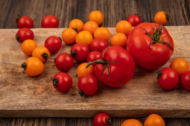 Draufsicht der organischen bunten Tomaten lokalisiert auf einem hölzernen Küchenbrett auf einer Holzwand