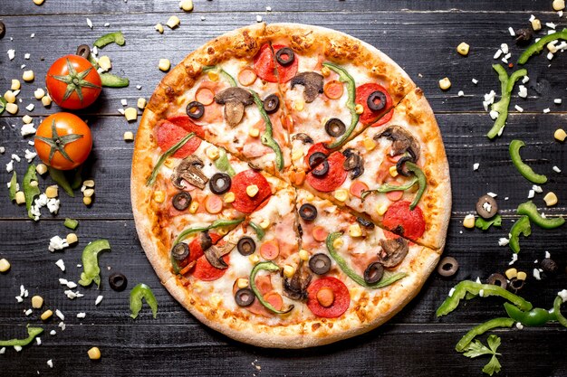 Draufsicht der Peperoni-Pizza mit Pilzwürsten Paprika-Olive und Mais auf schwarzem Holz