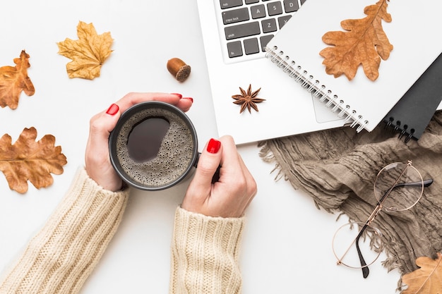 Kostenloses Foto draufsicht der person, die kaffeetasse mit notizbuch und laptop hält