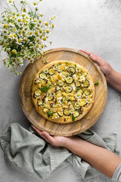 Draufsicht der Person, die köstliche gekochte Pizza mit Blumenstrauß der Kamille Blumen hält