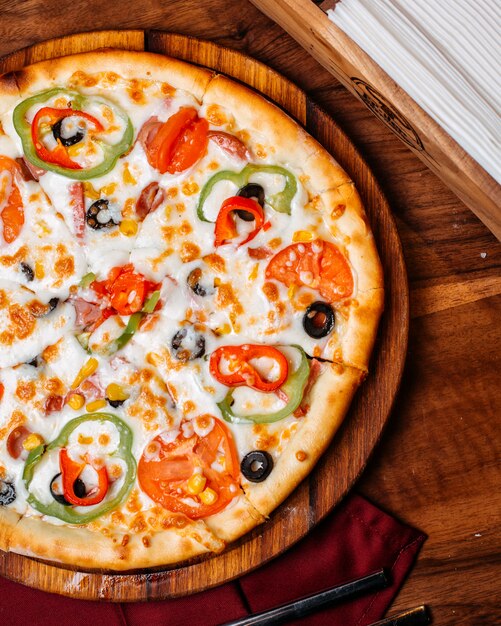 Draufsicht der Pizza gefüllt mit Tomaten bunte Paprika-Salami und Oliven auf einem Holzbrett