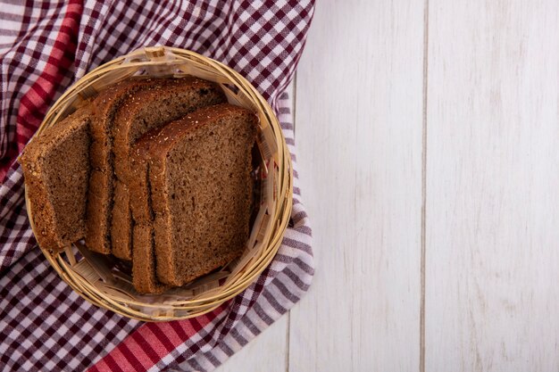 Draufsicht der Roggenbrotscheiben im Korb auf kariertem Stoff auf hölzernem Hintergrund mit Kopienraum