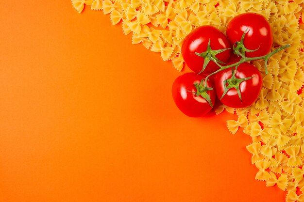 Draufsicht der rohen Nudelfarfalle mit einem Bündel Tomaten und Kopienraum auf Orange