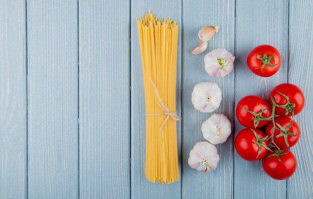 Draufsicht der rohen Spaghetti gebunden mit einem Seil mit frischem Tomatenknoblauch mit Kopienraum auf rustikalem Hintergrund