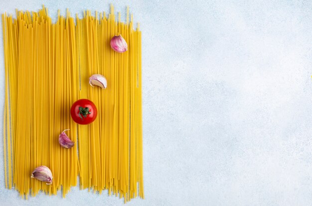 Draufsicht der rohen Spaghetti mit Tomate und Knoblauch auf einer grauen Oberfläche