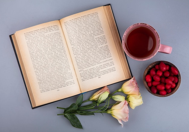 Draufsicht der roten frischen Kornelkirschenbeeren auf einer Schüssel mit einer Tasse Tee auf einem grauen Hintergrund