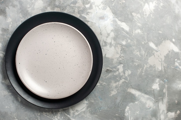 Draufsicht der runden leeren Platte schwarz gefärbt mit weißer Platte auf grauer Oberfläche
