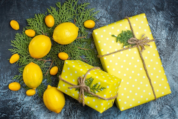 Draufsicht der Sammlung natürlicher organischer frischer Zitrusfrüchte auf Tannenzweigen und gelben Geschenkboxen auf dunklem Hintergrund