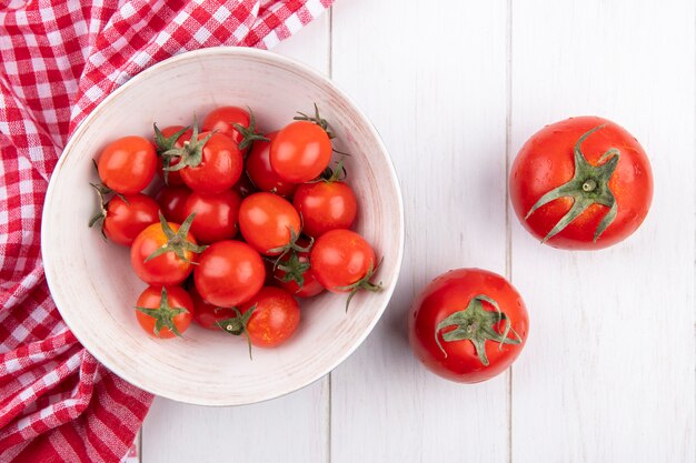 Draufsicht der Schüssel der Tomate auf kariertem Stoff und anderen auf Holz