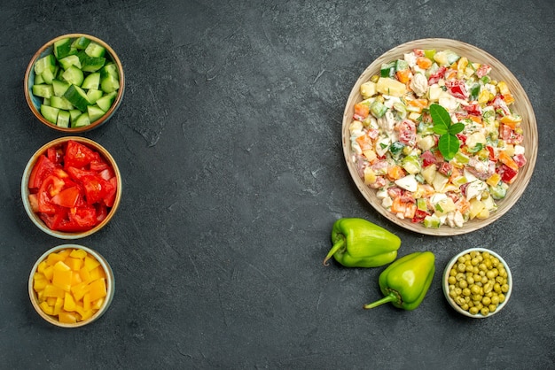 Draufsicht der Schüssel des Gemüsesalats mit Schüsseln des Gemüses und Paprika auf Seite auf dunkelgrünem Tisch