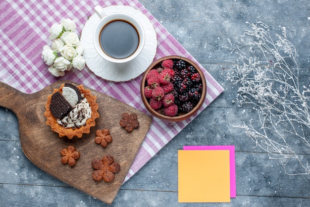 Draufsicht der Schüssel mit Beeren frischen und reifen Früchten mit Keksen und Kaffee auf grauem Schreibtisch, Beerenfrucht frisch reifen milden Wald