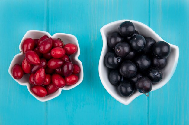 Draufsicht der schwarzen Trauben auf einer Schüssel mit Kornelkirschenbeeren auf einem blauen hölzernen Hintergrund