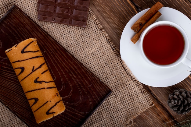 Draufsicht der Schweizer Rolle mit Aprikosenmarmelade auf einem Holzbrett, das mit einer Tasse Tee auf rustikal serviert wird