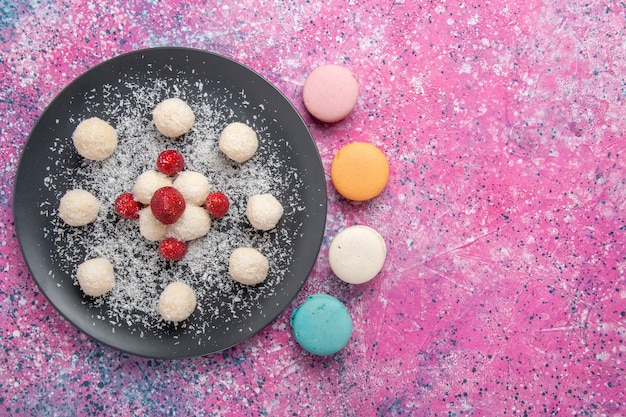 Draufsicht der süßen Kugeln der köstlichen Kokosnussbonbons mit französischen Macarons auf der rosa Oberfläche