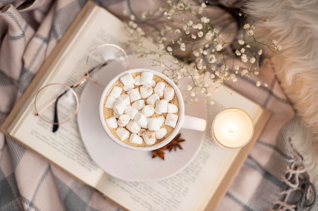 Draufsicht der Tasse heißen Kakaos mit Marshmallows auf Buch mit Gläsern und Kerze