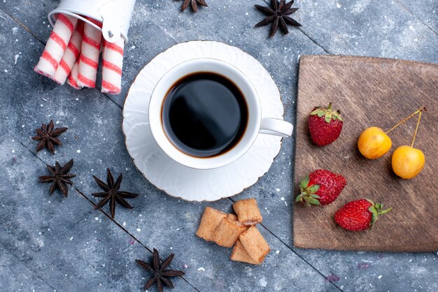 Draufsicht der Tasse Kaffee mit frischen roten Erdbeerplätzchen rosa Stockbonbons auf hellem Schreibtisch, Keksbonbon-Kaffeebeere