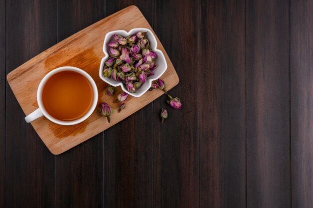 Draufsicht der Tasse Tee mit getrockneten Rosenknospen auf Tafel auf Holzoberfläche