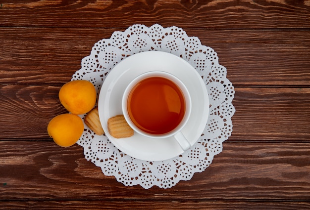 Draufsicht der Tasse Tee mit Keksen im Teebeutel und in den Aprikosen auf hölzernem Hintergrund