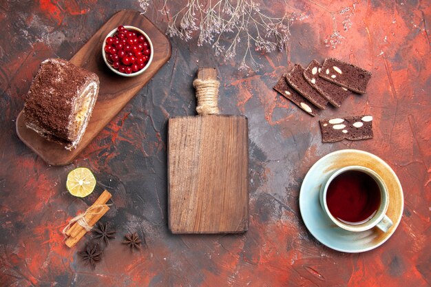 Draufsicht der Tasse Tee mit Kuchen- und Keksrollen auf dunkler Oberfläche