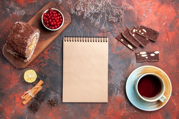 Draufsicht der Tasse Tee mit Kuchen- und Keksrollen auf dunkler Oberfläche