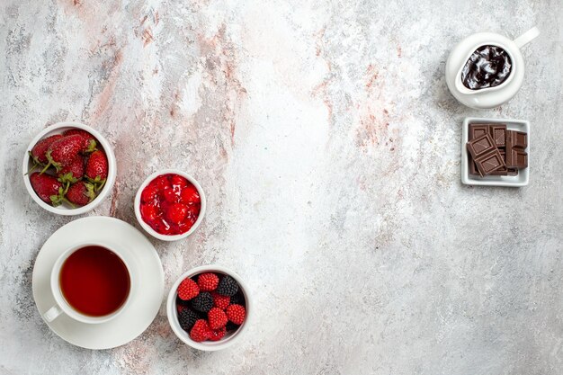 Draufsicht der Tasse Tee mit Marmeladenkonfekt und Schokolade auf einer weißen Oberfläche