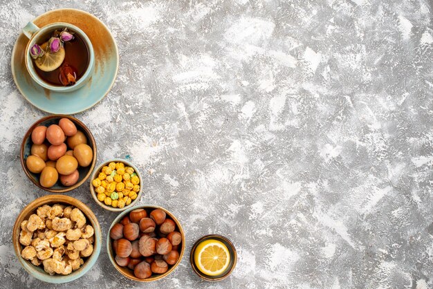 Draufsicht der Tasse Tee mit Nüssen und Bonbons auf weißer Oberfläche