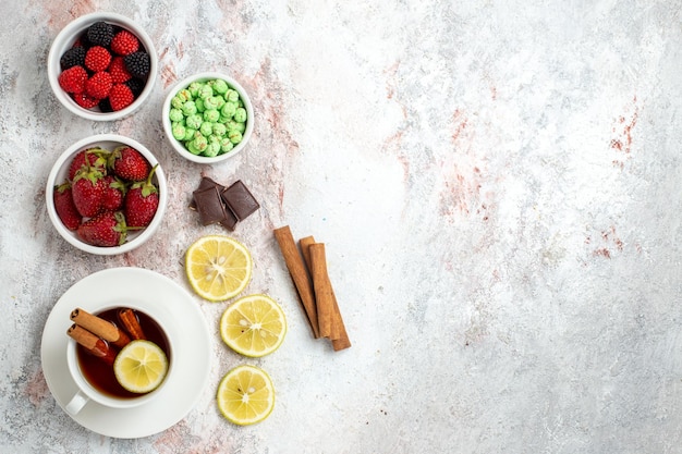 Draufsicht der Tasse Tee mit Süßigkeiten und Erdbeeren auf weißer Oberfläche